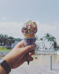 Cropped hand holding ice cream cone against sky