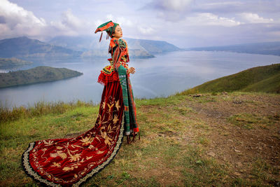 Woman wearing traditional clothing while standing on mountain against lake