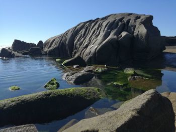 Rocks by sea against clear sky
