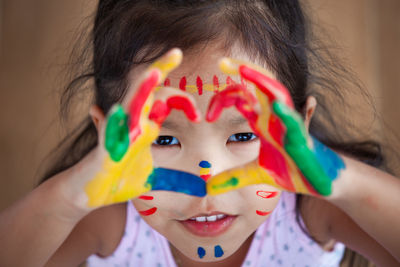 Close-up portrait of girl colorful body paint on hands making heart shape