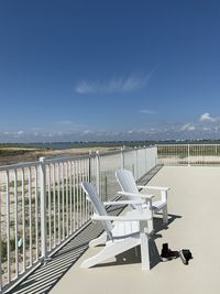 Empty chairs by railing against sky