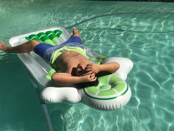 High angle view of boy relaxing on inflatable raft in swimming pool