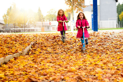 Girls riding push scooters at park during autumn