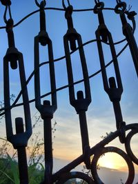 Low angle view of metal fence against sky during sunset