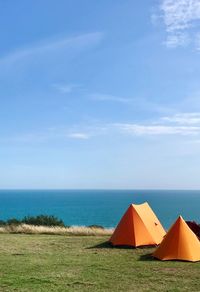 Scenic view of orange camping tents and sea against blue sky