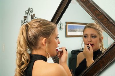 Young woman looking in mirror while applying lipstick at home