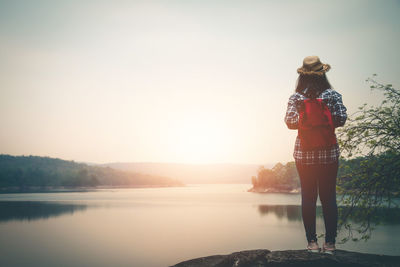 Woman standing by lake against sky during sunset