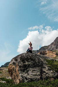 Low angle view of woman sitting on mountain against sky