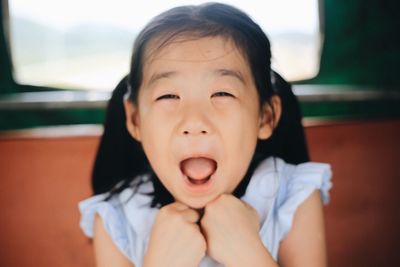Close-up portrait of girl screaming while sitting by window at home