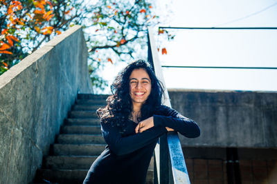 Portrait of smiling young woman standing against railing