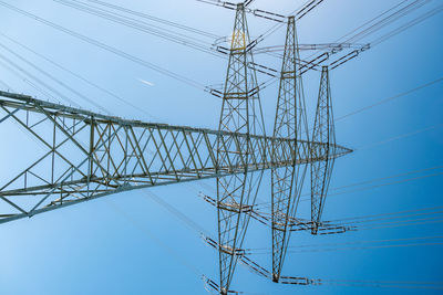 Low angle view of electricity pylon against clear blue sky