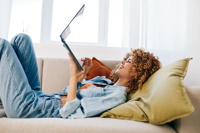 Young woman using mobile phone while lying on bed at home