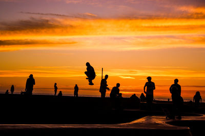 Silhouette people on beach against orange sky