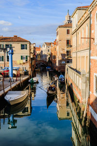 Boats moored in canal amidst buildings in city