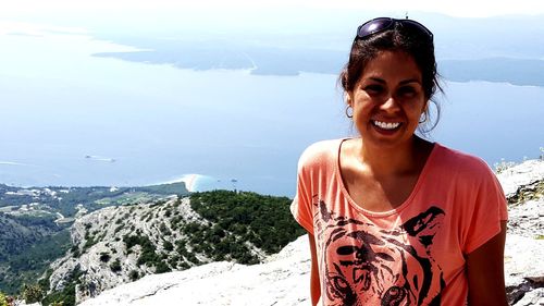 Portrait of smiling young woman standing on mountain against sky