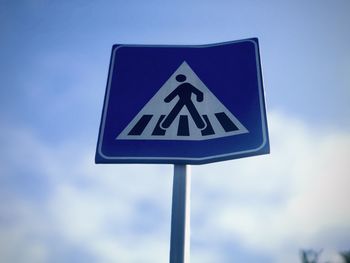 Low angle view of road sign of pedestrian crossing against blue sky