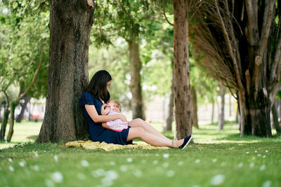 Full length of woman sitting by tree at park