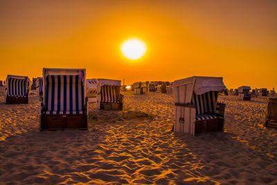 Hooded chairs on beach against sky during sunset