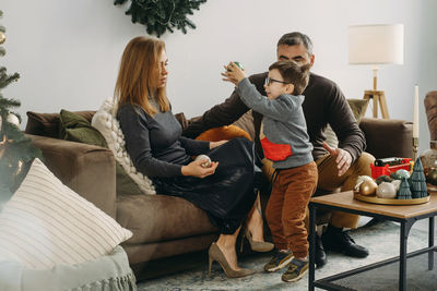 Family with child playing near christmas tree. child unpacking gifts, parents enjoy christmas tree