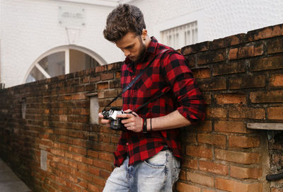 Handsome man with camera standing against brick wall