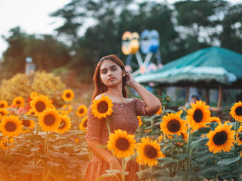 Portrait of young woman with yellow flowers against plants