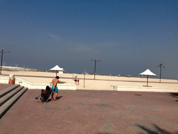 Shirtless man walking with baby carriage at beach