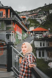 Portrait of woman standing by railing against buildings in city