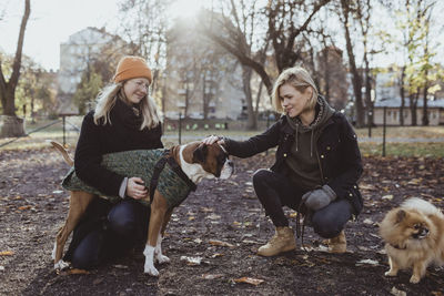 Women crouching while stroking boxer dog at park during autumn