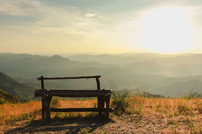 Empty bench on field against sky during sunset