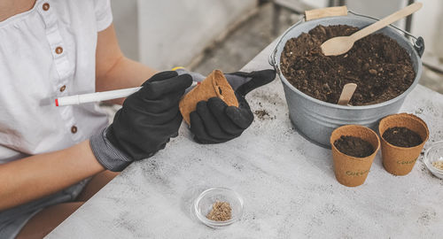 Caucasian teenage girl in gardening gloves signs a cardboard glass with a marker.