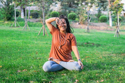 Young woman is sitting in the lotus position and doing breathing exercises in a park.