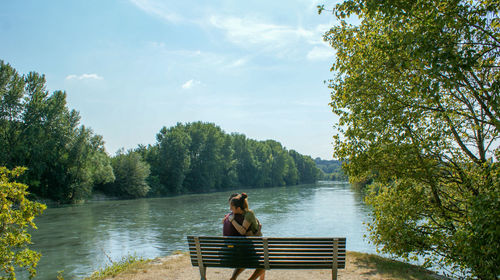 Man sitting by lake against sky