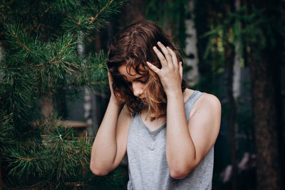 Young woman looking away while standing against trees