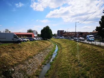 Road amidst field and city against sky