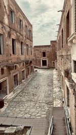 Empty alley amidst buildings in city against sky
