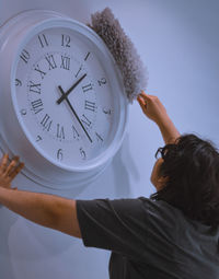 Portrait of a girl cleaning up a big white clock at the wall 