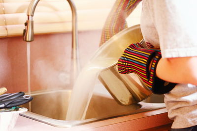 Midsection of woman pouring water from container in kitchen sink at home