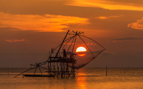 Silhouette cranes against orange sky during sunset