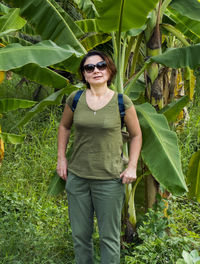 Portrait of woman wearing sunglasses while standing against banana tree