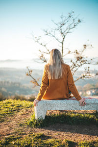 Rear view of woman sitting on field against sky