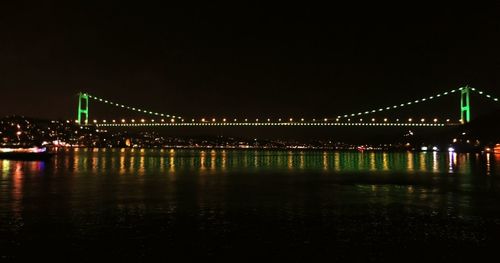 Illuminated bridge over river against sky at night