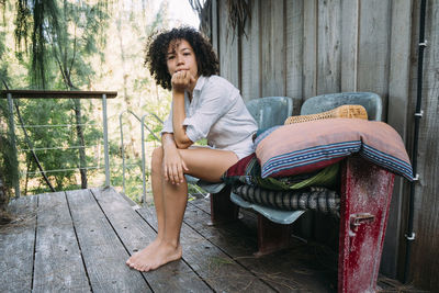 Portrait of woman with hand on chin while sitting on chair in balcony