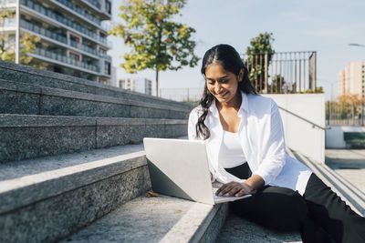 Smiling young woman using laptop on steps