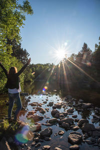 Rear view of woman with arms raised standing on rocks by lake