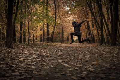 Woman jumping on dirt road amidst trees in forest