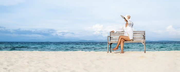 Rear view of woman sitting on beach against sky