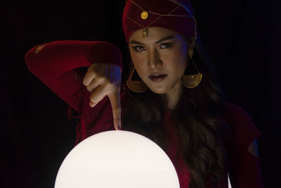 Portrait of female fortune teller pointing at sphere against black background