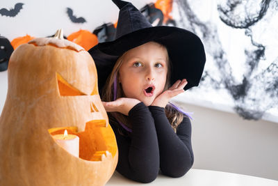 Cute girl in costume of witch with pumpkin at home, having fun, celebrating halloween