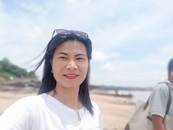 Portrait of smiling young woman on beach against sky