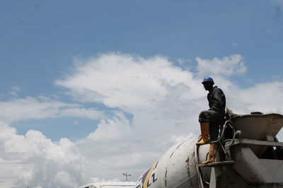 Low angle view of construction worker standing on cement truck against sky
